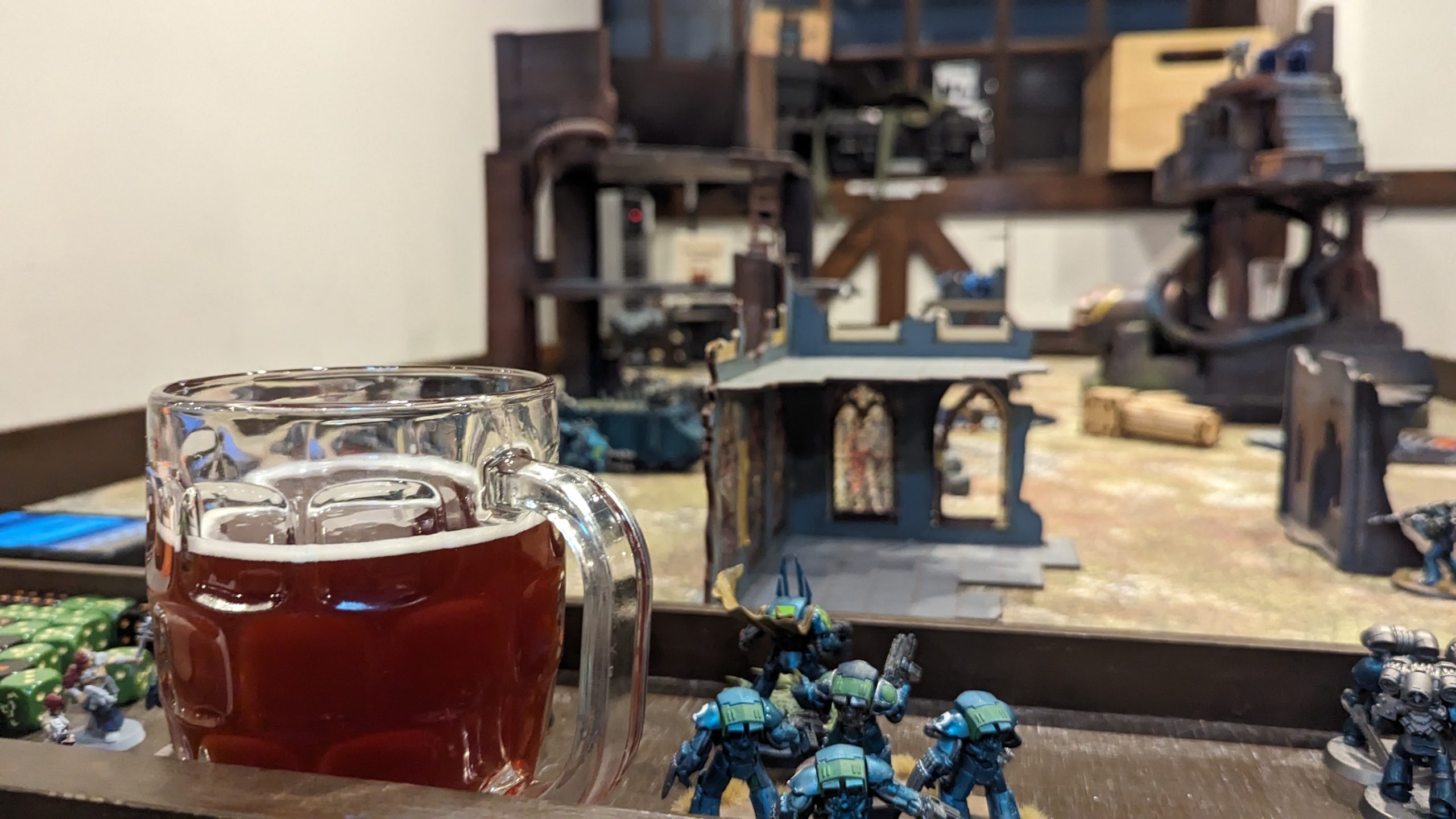 A pint of beer beside painted miniatures and terrain on a gaming table at Emerald Tavern Games & Cafe