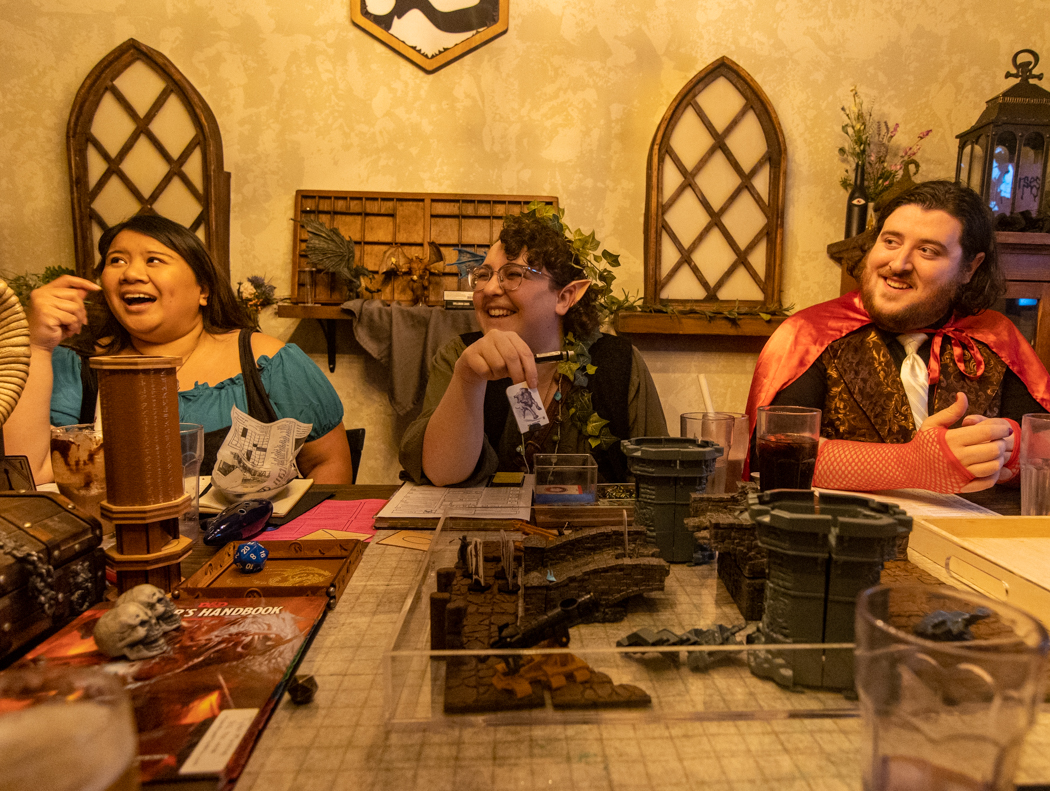 Players in costume laughing around a DnD table with terrain and miniatures at Vigilante Gastropub & Games